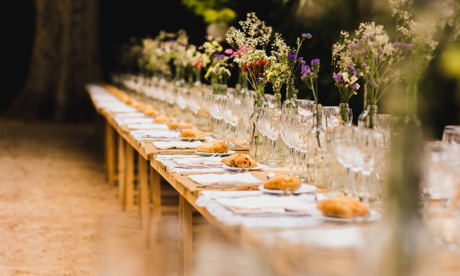 Long banquet table set with wildflowers and glassware for a wedding reception